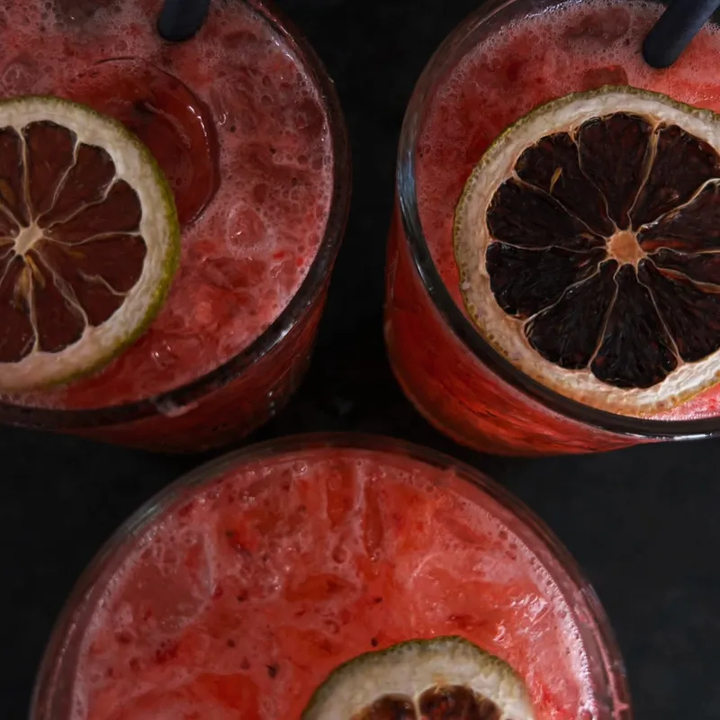 Três copos de bebida vermelha com rodelas de laranja, vistos de cima.