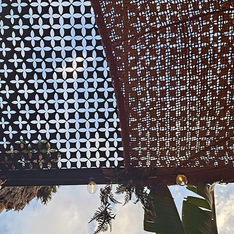 Painel de metal recortado e pérgola de vime contra o céu, na esplanada.